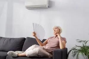 Senior Woman Fanning Herself On Couch In Summer Heat