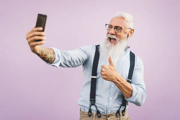 Senior Man Using Mobile Smartphone And Listening Music With Airpods - Happy Man Having Fun With New Trends Technology Social Media Apps - Elderly Lifestyle.