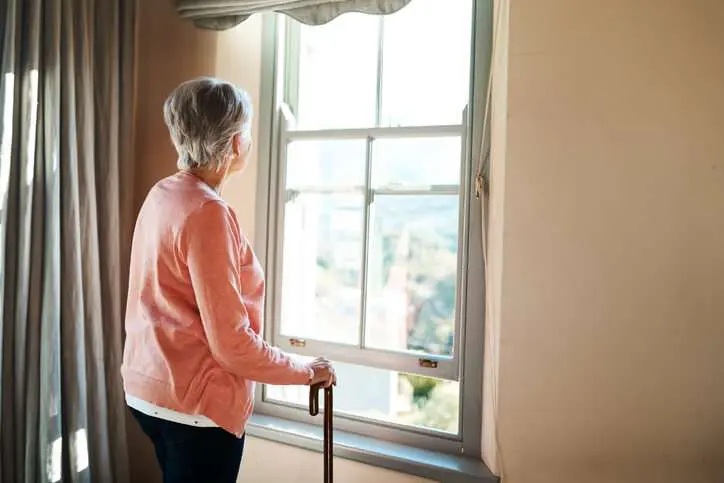 Senior Woman With Walking Cane Looking Out Of The Window