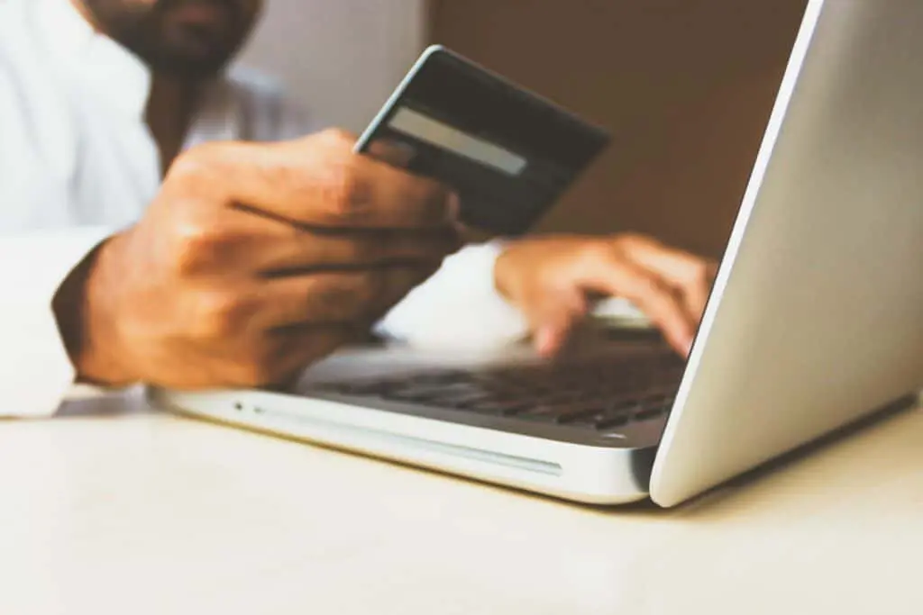 A Person Holding Credit Card While Usinh Laptop