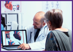 Questions For Your Cardiologist: What Heart Patients Should Ask &Raquo; Photo Of A Female Patient Sitting At A Desk With A Male Cardiologist Who Is Showing Her Images Of A Heart Of A Laptop Canva Border Added 1 300X214 1