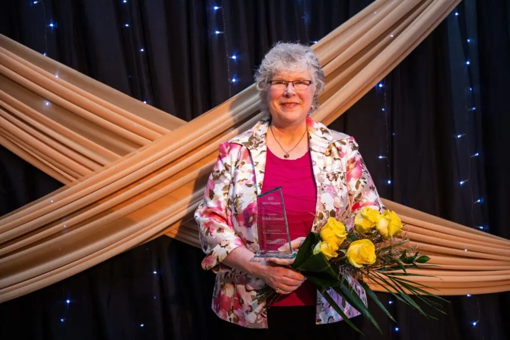 Woman Standing In Front Of Ribbons Crossed In An X, With Flowers And An Award