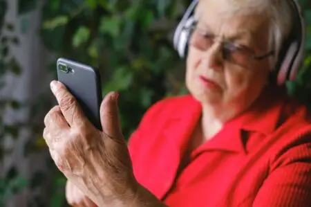 An Elderly In A Red Shirt Using A Phone While Wearing Headphones