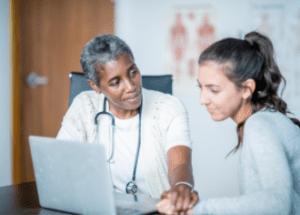 The Importance Of Shared Decision-Making In Healthcare &Raquo; Photo Of A Black Female Doctor Speaking With A White Young Female Patient With Her Hand On The Patients Arm New Canva 1 E1674688177104 300X215 1