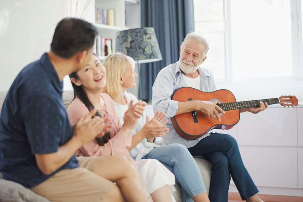 Senior Man Playing Guitar With Group Clapping Along