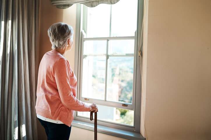 Senior Woman With Walking Cane Looking Out Of The Window