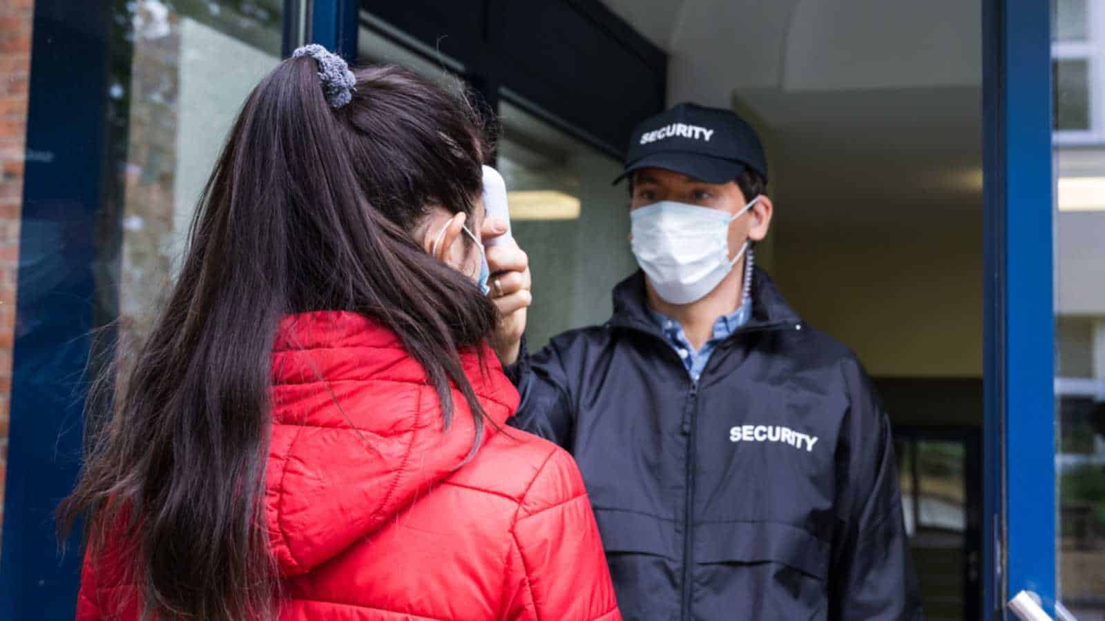 Security Guard Checking Temperature At Building Entrance