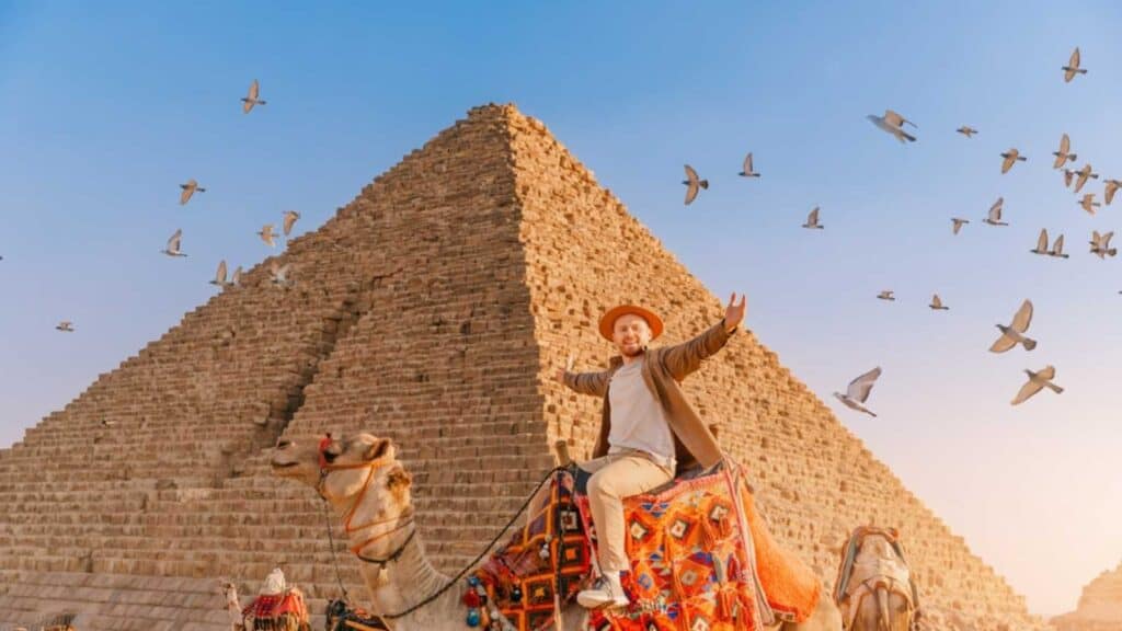 Tourist Man With Hat Riding On Camel Background Pyramid Of Egyptian Giza, Sunset Cairo, Egypt.