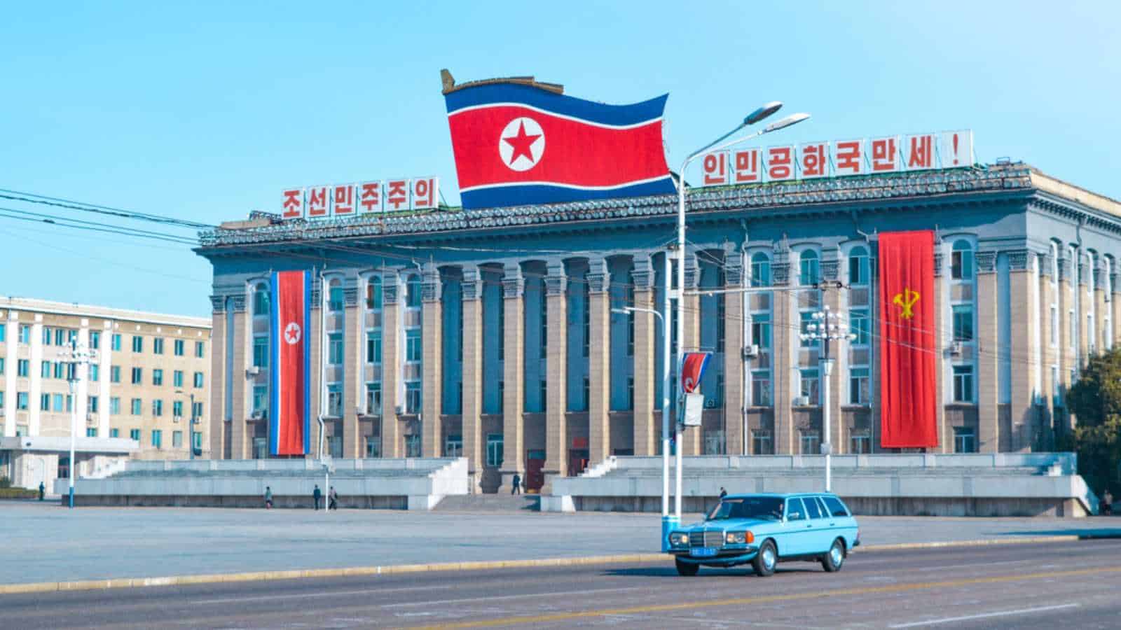 Pyongyang, North Korea - October 9, 2019: Old Blue Car Driving In Pyongyang Street With North Korea Flag