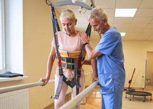 Tips For Recovering From A Stroke &Raquo; Photo Of A Male Physical Therapist Helping A Woman Walk While She Is Secured In An Overhead Harness Canva 1 300X215 1