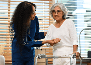 What You Need To Know About Strokes &Raquo; Photo Of An Older Female Stroke Survivor Standing By A Walker Getting Help From A Nurse Or Therapist Canva 1 300X214 1