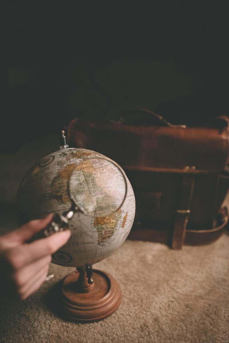 Person Holding Magnifying Glass Near Desk Globe