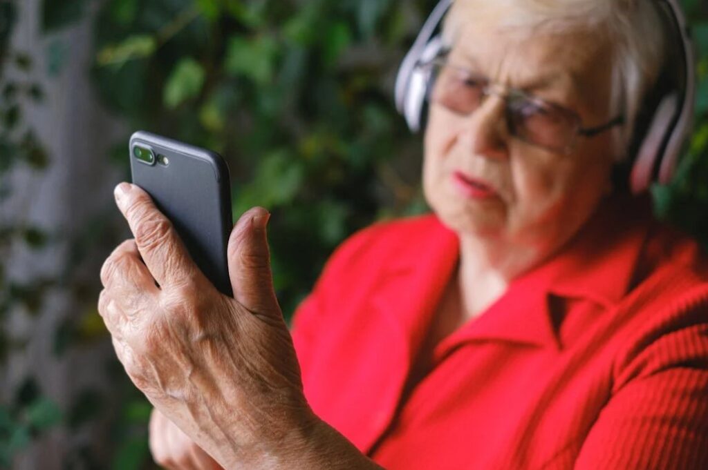 An Elderly In A Red Shirt Using A Phone While Wearing Headphones